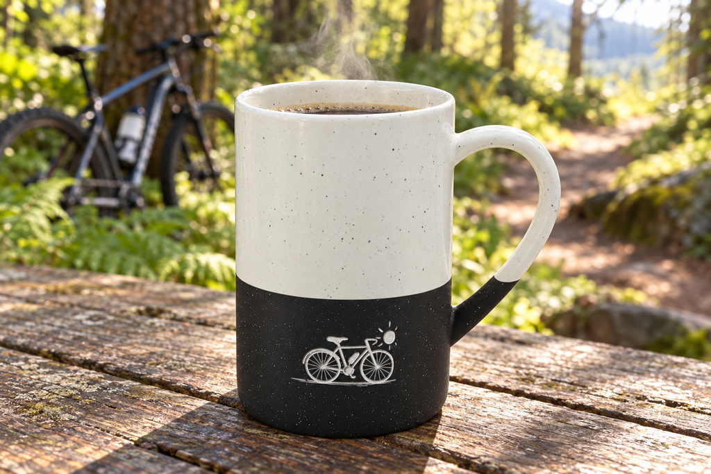 Minimal bicycle engraved speckled mug on a picnic table by a forest trail